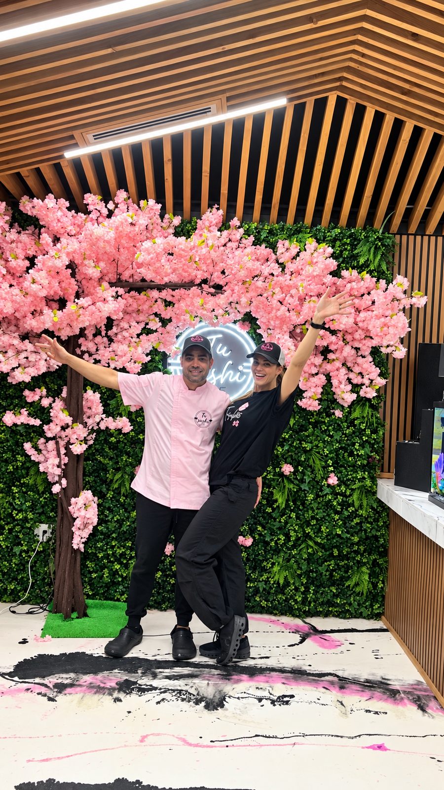 Genesis Perera y Angel Mendoza en Tu Sushi 305 frente a la decoración de cerezos.