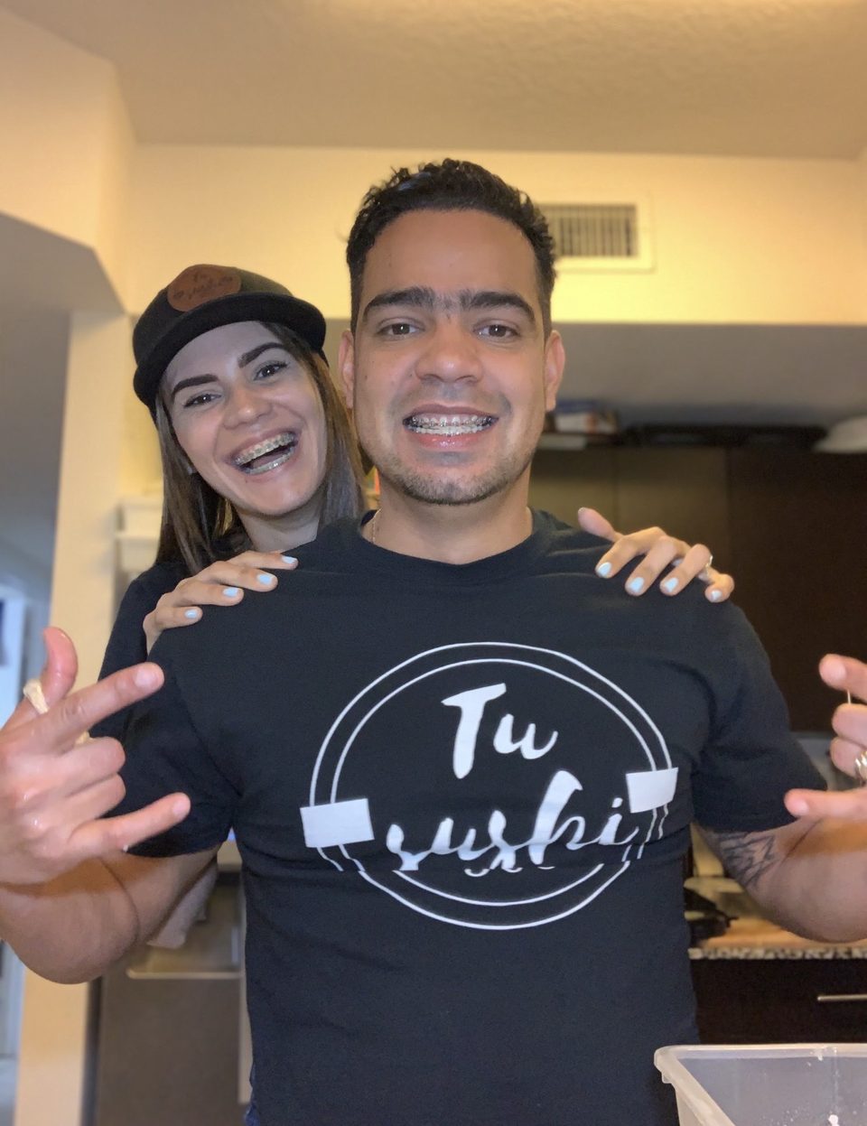Genesis Perera y Angel Mendoza sonriendo en casa, él con la camiseta de Tu Sushi 305.